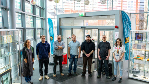 Grŵp o artistiaid yn sefyll yng nghyntedd Adeilad Alex â waliau gwydr.