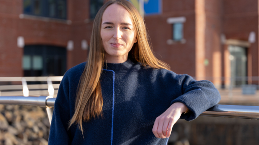 A happy smiling woman in a navy blue top standing outside a building.