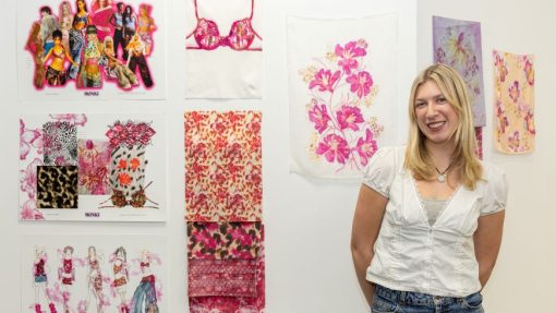 A happy smiling student standing proudly in front of her colourful work.