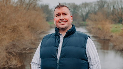man standing smiling at camera with river and trees in background