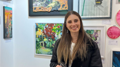 A happy smiling student pictured in front of a wall displaying her textiles work.