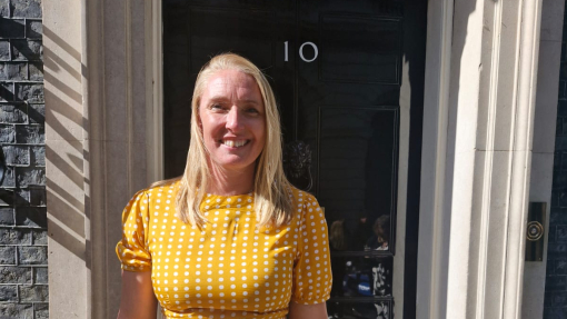 A smiling lady in a yellow dress standing outside the famous black door with number 10 on it.