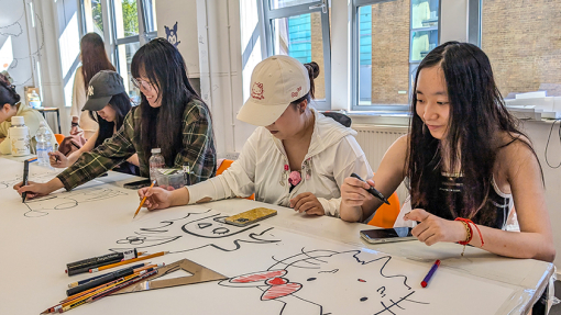 Students sitting at a large white desk using their creative skills.