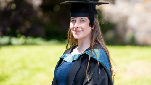 Chloe Fowler in graduation gown in front of old building at UWTSD Carmarthen