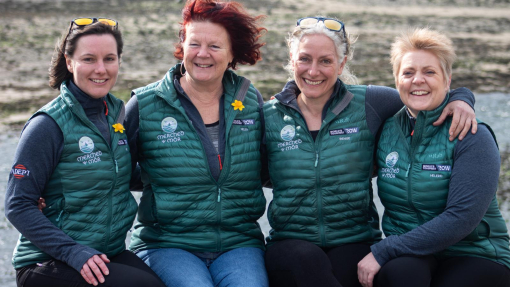 Four ladies wearing branded tops sitting in front of a wall.