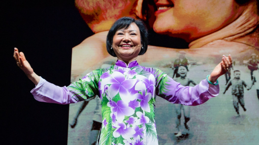 Phan Thị Kim Phúc (Kim) with hands out during speech with the iconic image in the background