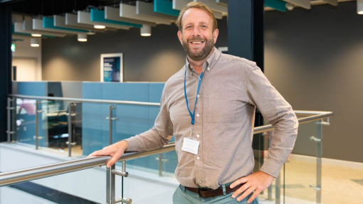A man standing against a glass bannister.
