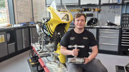 A student sitting in a workshop surrounded by engineering parts.