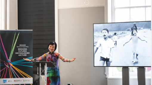 Phan Thị Kim Phúc on stage at Bridging Futures event with the famous picture of her as a child on screen in the background