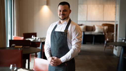 A chef wearing a navy apron, standing proudly in a catering venue.
