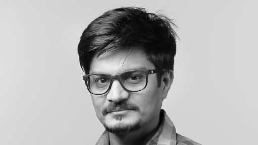 A mono image of a lecturer in a checked shirt, wearing glasses.