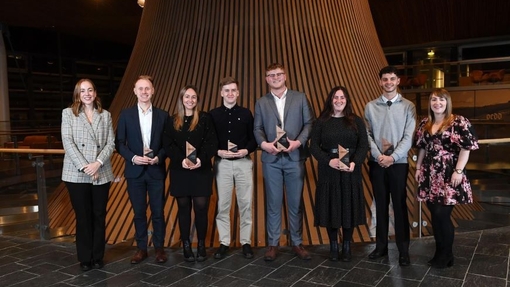 A proud group of student winners standing in front of a brick wall.