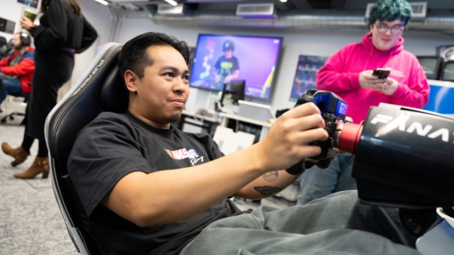 A man seated in a gaming chair concentrating on a screen, holding controllers in his hand.