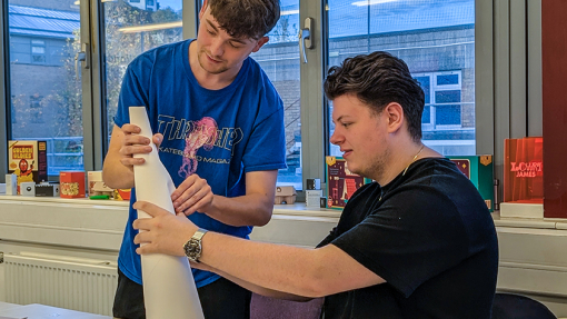 Two students, one seated and the other standing concentrating on a creative task.