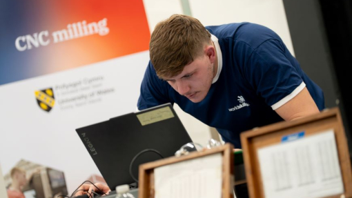 A student looking closely at a laptop in a workshop environment, with a competition branded background.