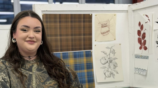 A student sitting at her desk in a workshop with creative work on show.