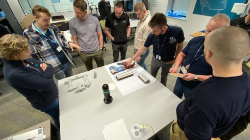 A group of people standing around a white table in a workshop.