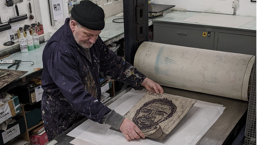 An artist working on a printing machine in a workshop.
