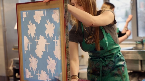 A student wearing a green apron with her creative art work.