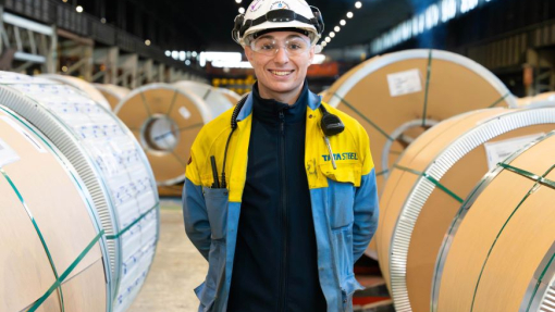 A smiling graduate dressed in protective clothing standing in a work environment.