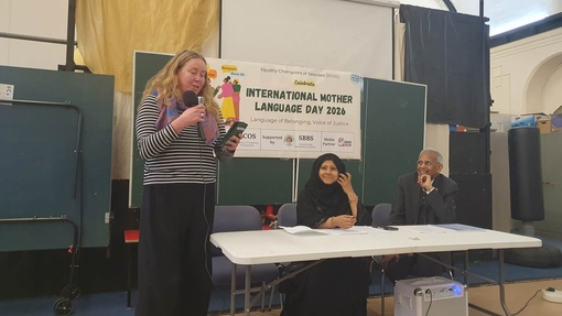 Jesscia Pitman standing up in the front of the hall with International Mother Language Day banner in the background