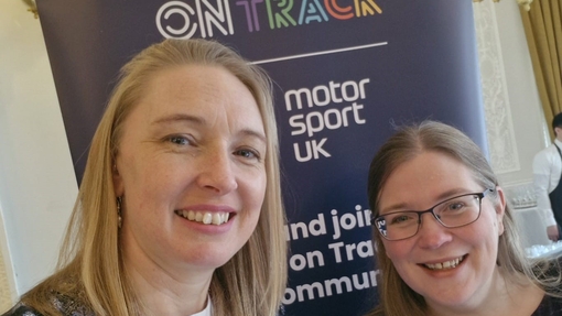 Two smiling women standing in front of a navy blue branded banner.