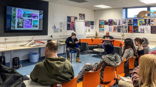 A packed lecture room of students listening to an artist sitting at the front of the room.