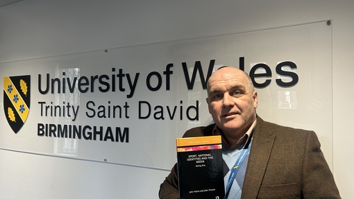 Dr John Harris with his book in front of UWTSD Birmingham sign