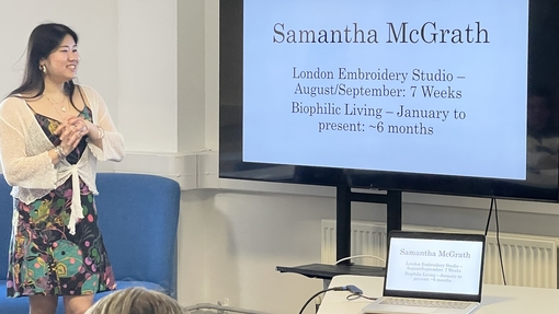 A girl smiling in front of audience, looking at a large display screen reading 'Samanth McGrath'