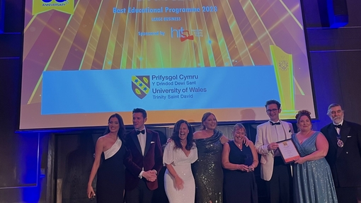 A group of staff and students in evening dress celebrating against a branded background.