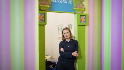 A lecturer standing against a poster on a wall with a colourful background.
