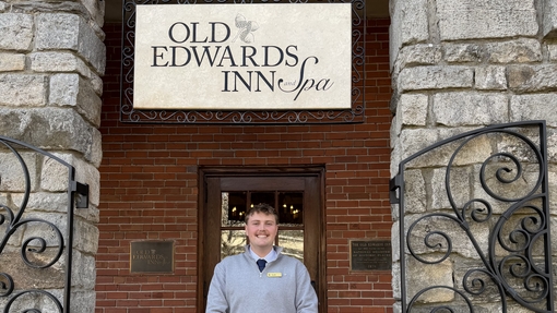 A man standing in front of an entrance with sign above his head reading 'Old Edwards Inn'