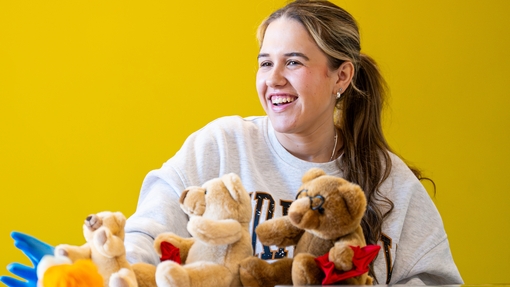 A smiling girl sitting with teddy bears on desk in front of her