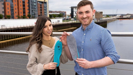 Two people standing on a bridge with a maritime theme behind them, holding onto two soles.