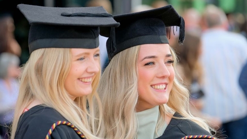 Two graduates in their caps and gowns smiling and posing for a photograph.