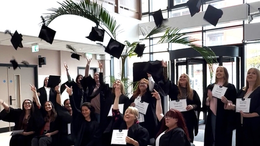 A large group of people dressed in cap and gowns celebrating by throwing their hats into the air.