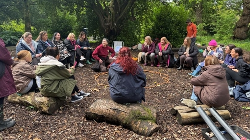 A large group sat in a circle in a woodland.