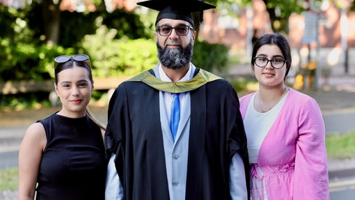A proud dad dressed in cap and gown with two of his daughters.