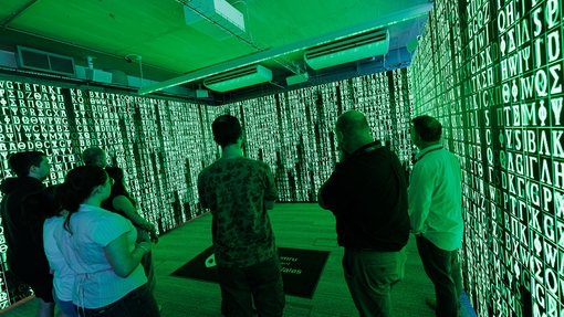 Studetns in immersive room with green colours on screen and ancient letters