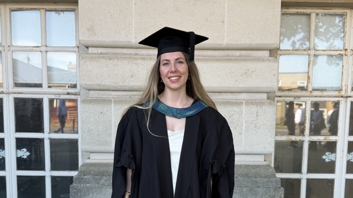 A woman standing in front of building in gap and gown on graduation day