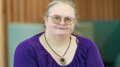 A lady wearing glasses and a purple top and a necklace.