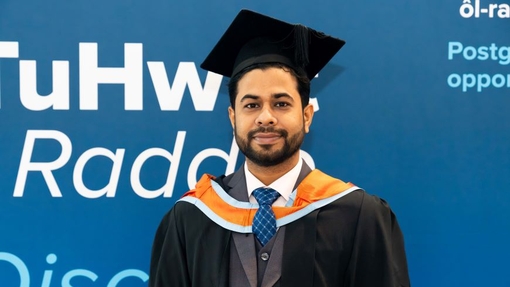 A smiling and proud graduate standing in his cap and gown.