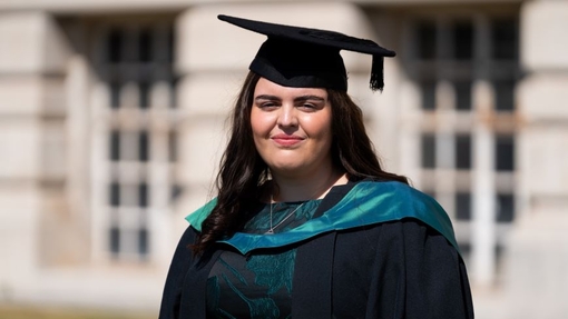 A smiling and proud graduate standing in her cap and gown.