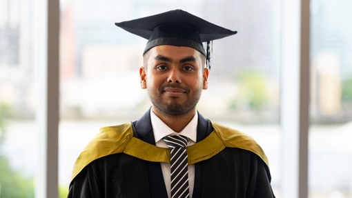 A smiling and proud graduate standing in his cap and gown.