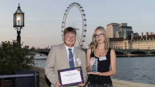 Two students standing on the terraces at the House of Commons in London, with the London eye in the background.
