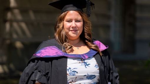 A smiling and proud graduate standing in her cap and gown.