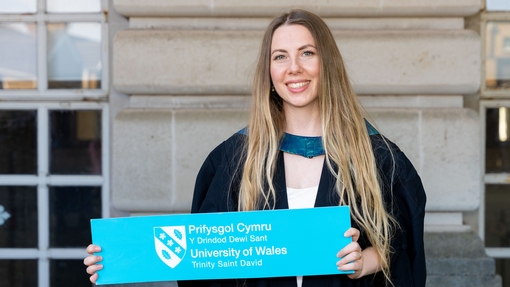 A woman holding a sign saying UWTSD