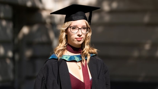 A smiling and proud graduate standing in her cap and gown.
