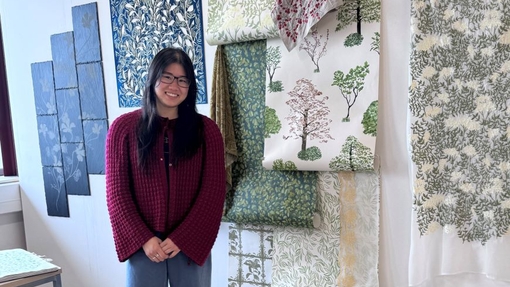 A student standing proudly in front of vibrant art work on a white wall.