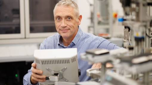 A man in a blue shirt, sitting close to robotics machinery.